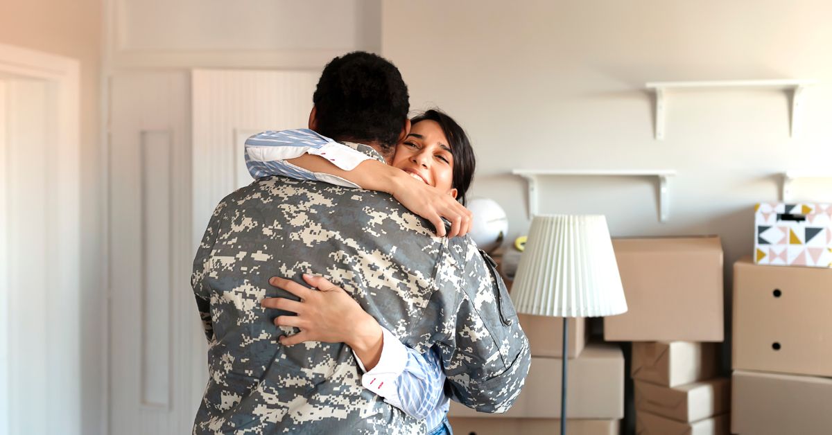 A veteran, with a heartwarming smile, tightly embraces his wife, both overwhelmed with joy, as they stand in front of their new home. Their hug symbolizes the realization of a dream and the sense of accomplishment that comes with becoming homeowners.